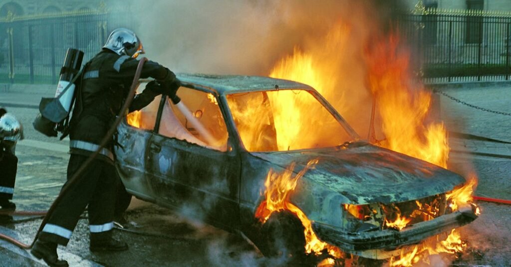 Firefighters extinguish a burning car in an urban setting, showcasing emergency response