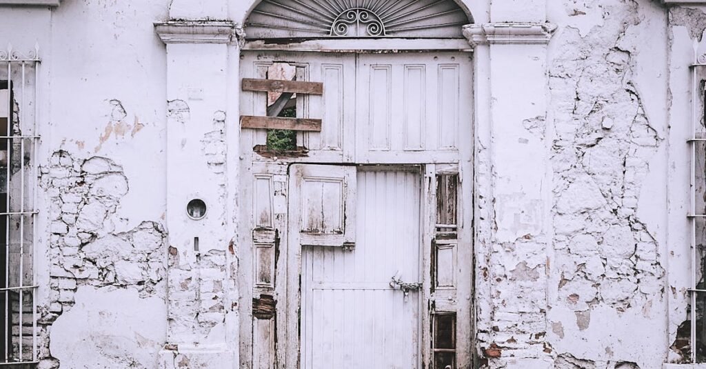 An old, decaying white building with a weathered door and cracked walls.
