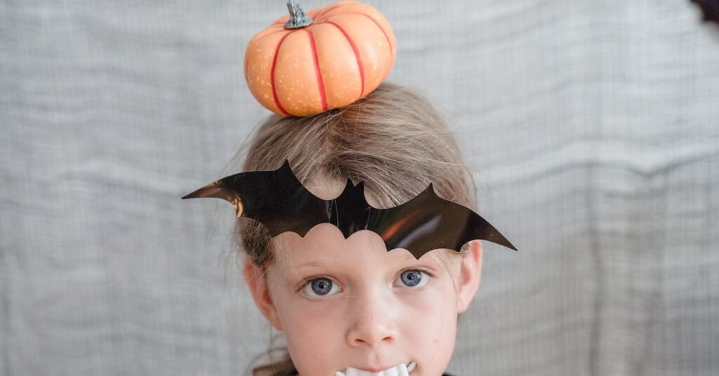 Young child dressed for Halloween with a bat-themed disguise and pumpkin accessory indoors.