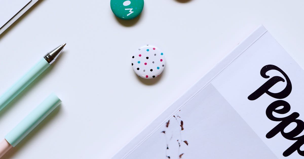 Flat lay of a contemporary desk setup with keyboard, pens, buttons, and a magazine on a white background.