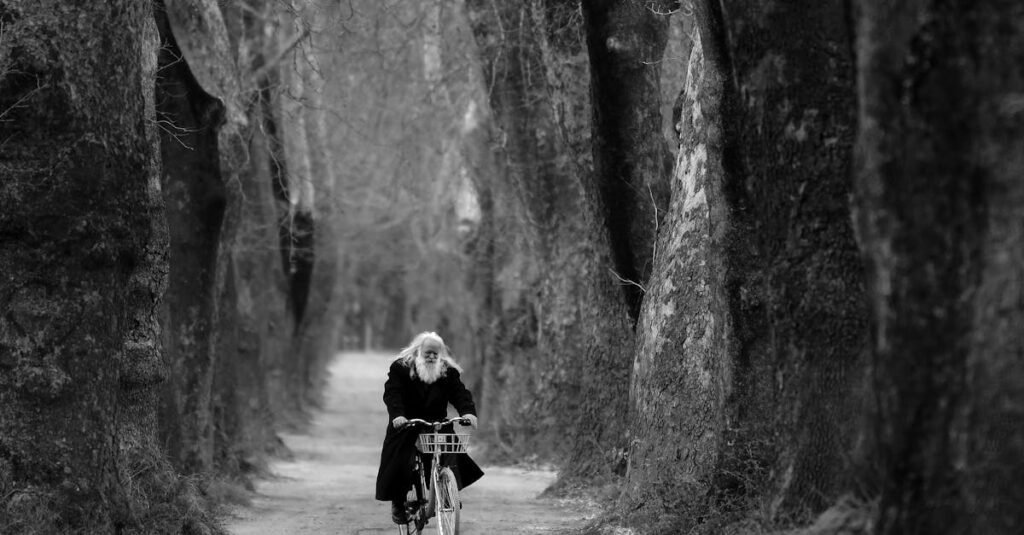 A senior man with a beard cycling through a tree-lined path in winter.