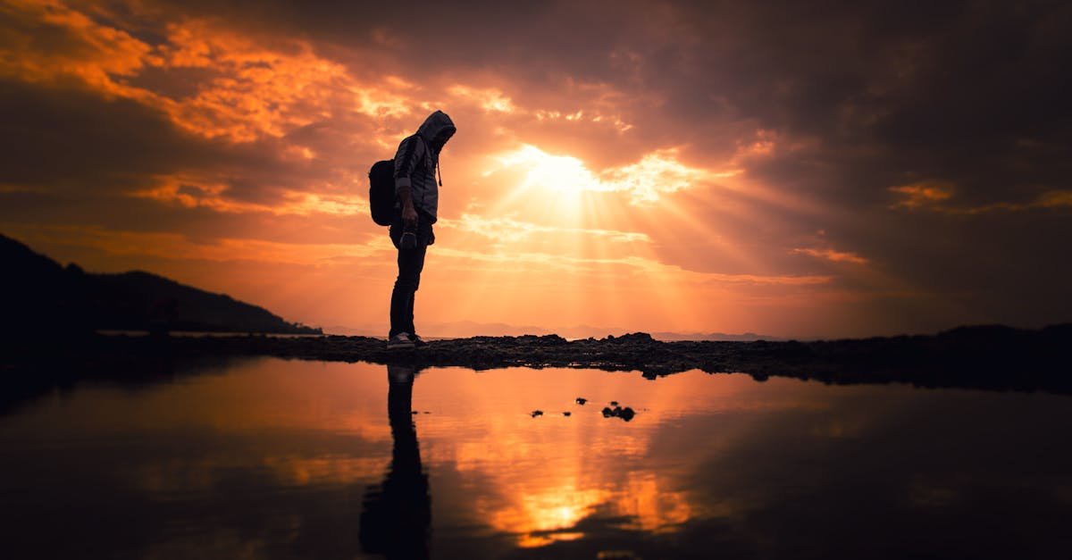 A lone hiker silhouetted against a vibrant sunset over a reflective lake in Korgan, Turkey.