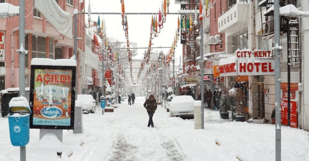 Winter scene in Malatya with people walking under a snowy arch and colorful umbrellas.