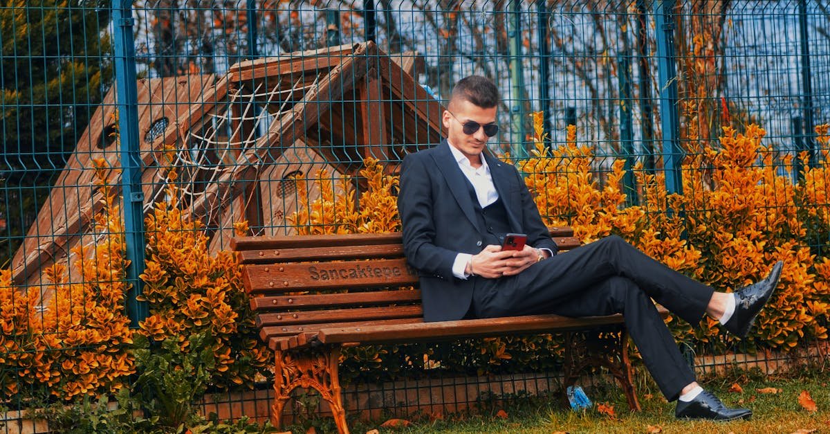 A stylish man in sunglasses sitting on a bench in autumn, using a smartphone.