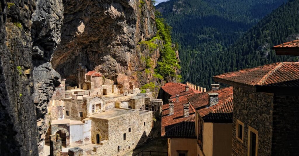 Historic stone monastery nestled among lush mountains and rocky cliffs.