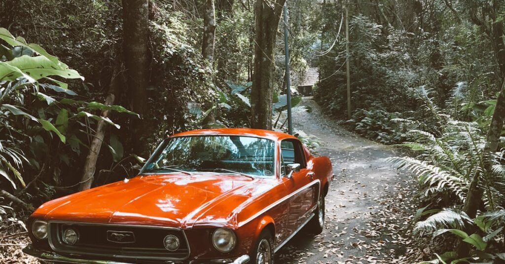 Vintage red car parked on a forest road surrounded by lush greenery.
