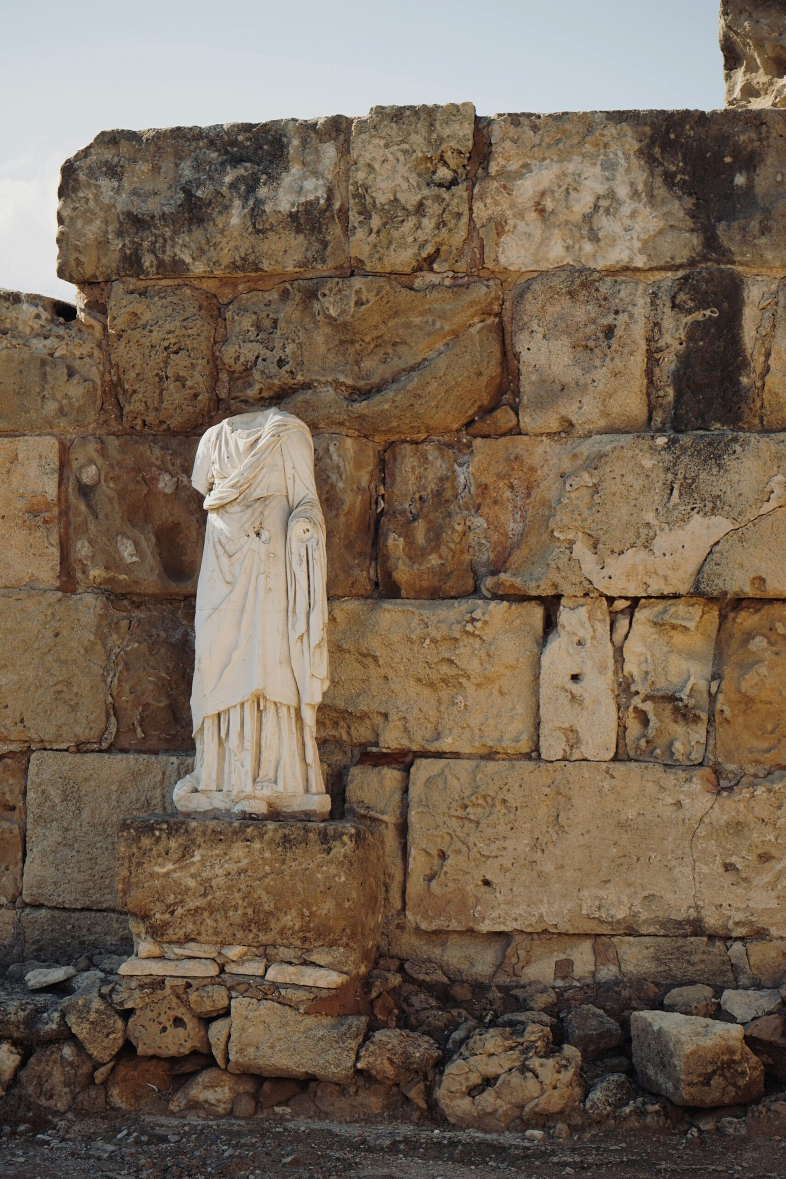 An ancient statue in Kıbrıs stands against a historic stone wall.