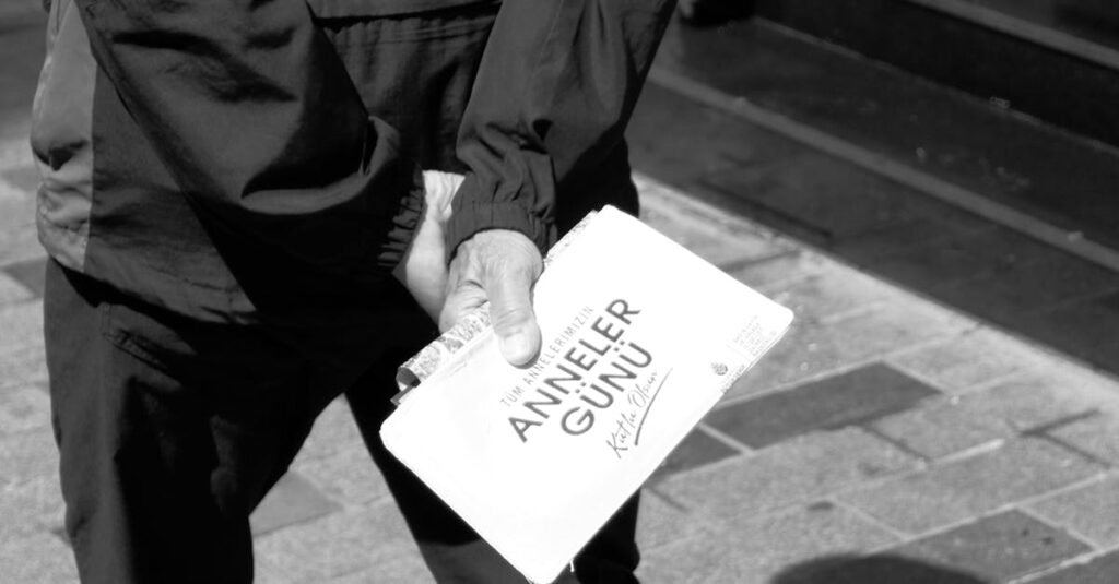 Man walking in İstanbul holding 'Anneler Günü' sign in black and white.