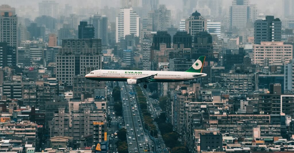 A passenger airplane flying over Taipei's skyline with modern urban buildings and cloudy skies.