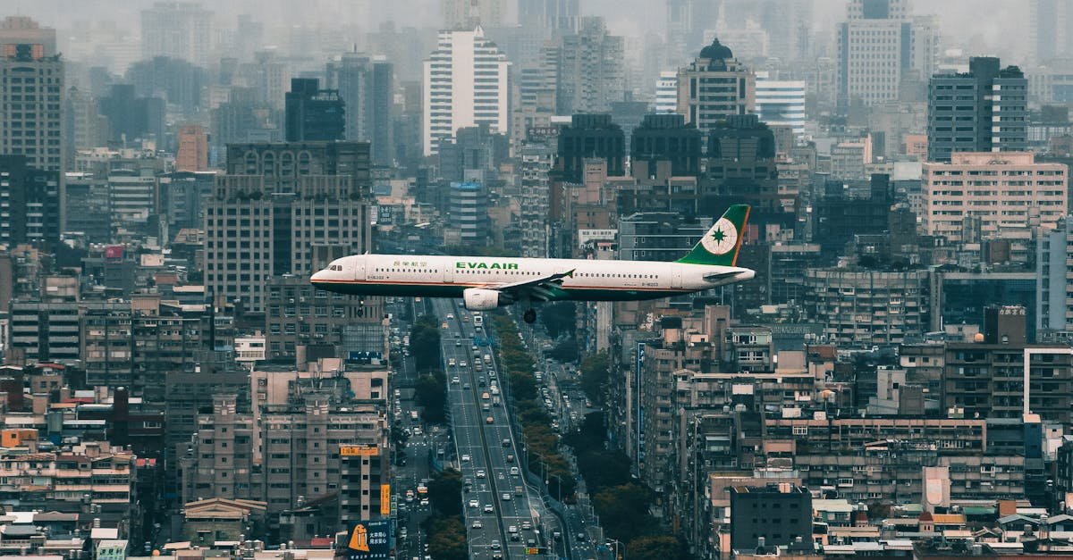 A passenger airplane flying over Taipei's skyline with modern urban buildings and cloudy skies.