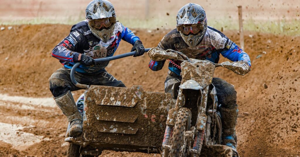 Two bikers maneuver a sidecar during an intense motocross race on a muddy track.
