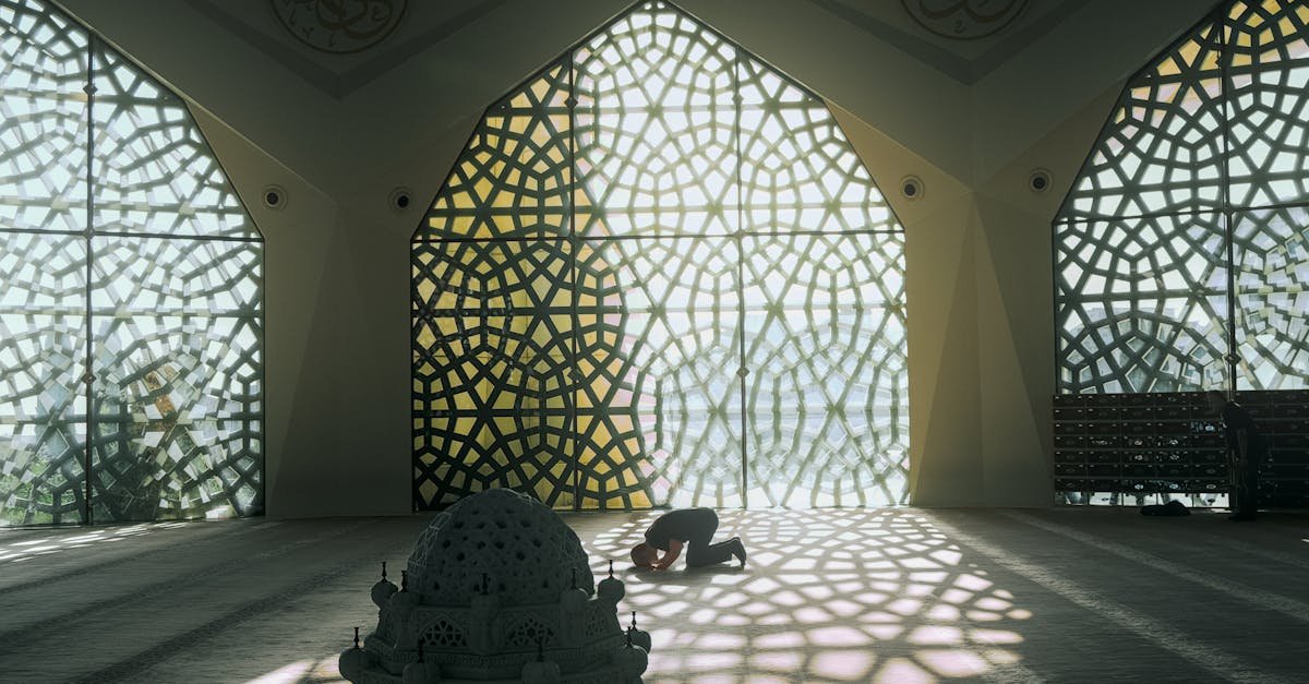 Silhouette of a person praying inside a mosque with intricate geometric designs.
