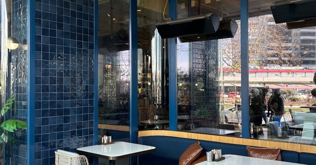 A chic cafe with blue tiles and large windows, offering an inviting and sunny space for diners.