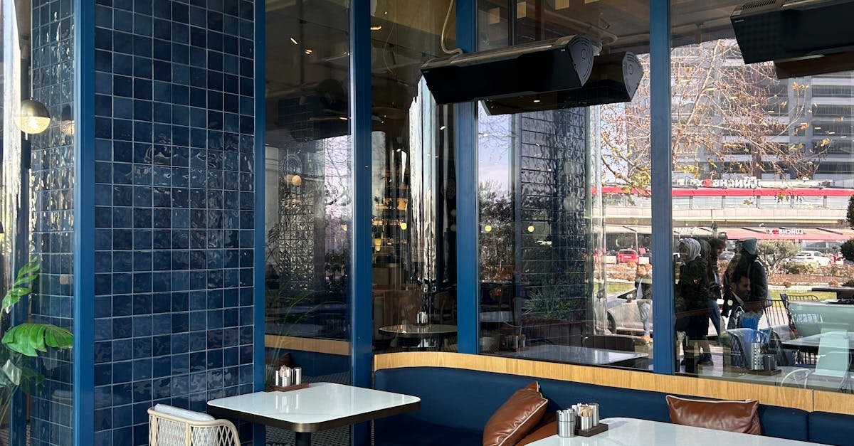 A chic cafe with blue tiles and large windows, offering an inviting and sunny space for diners.