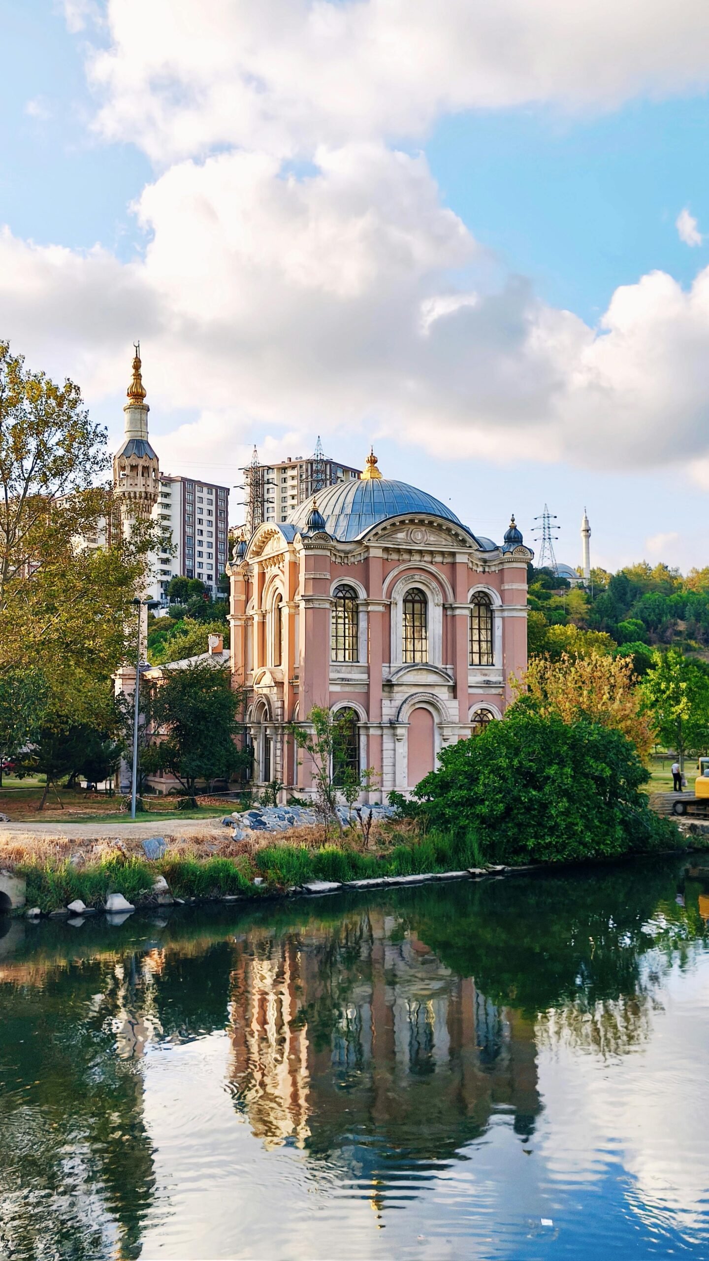 Picturesque view of a historic mosque by the river in İstanbul, Türkiye, with clear reflections and lush surroundings.