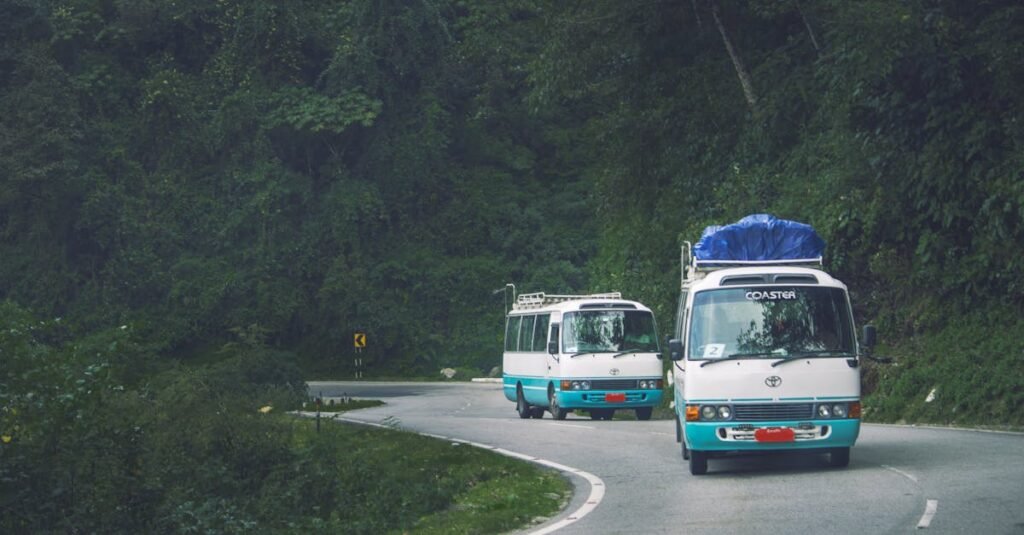 Two mini buses travel a scenic mountain road in Phuentsholing, Bhutan, surrounded by lush green forests.