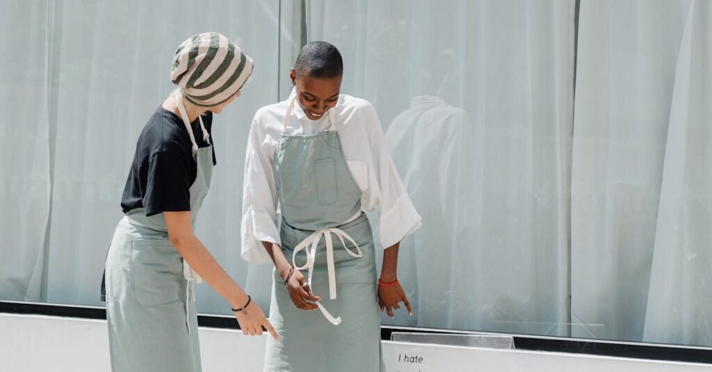 Two colleagues wearing aprons conversing in front of a cafe window during the day.