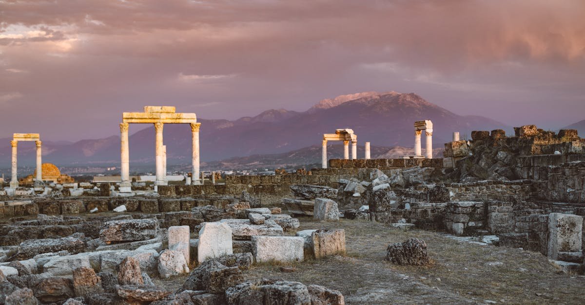 Explore ancient stone ruins and columns against a mountain backdrop during a stunning Turkish sunset.