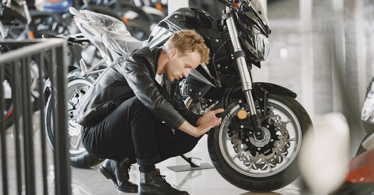 Stylish man inspecting motorcycle tire in a showroom wearing a black leather jacket.