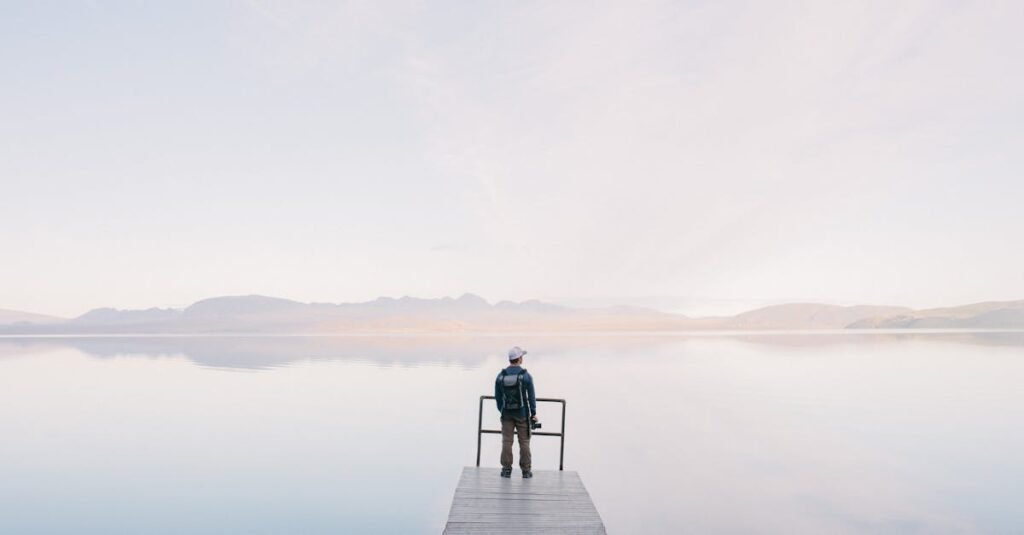 A solitary traveler stands on a dock enjoying the serene water view
