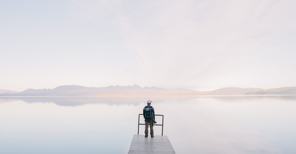 A solitary traveler stands on a dock enjoying the serene water view
