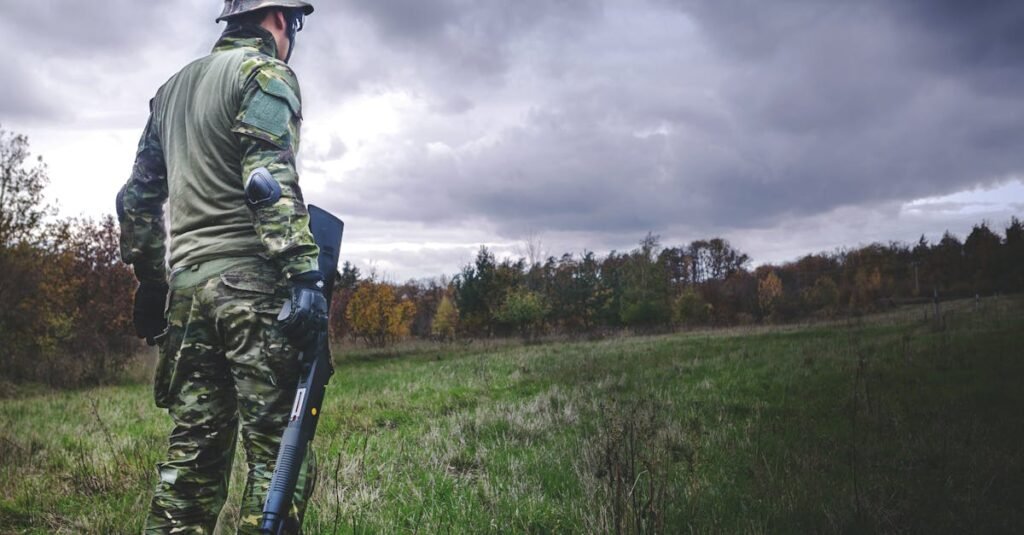 A soldier in camouflage with a rifle stands in a grassy field under a cloudy sky.