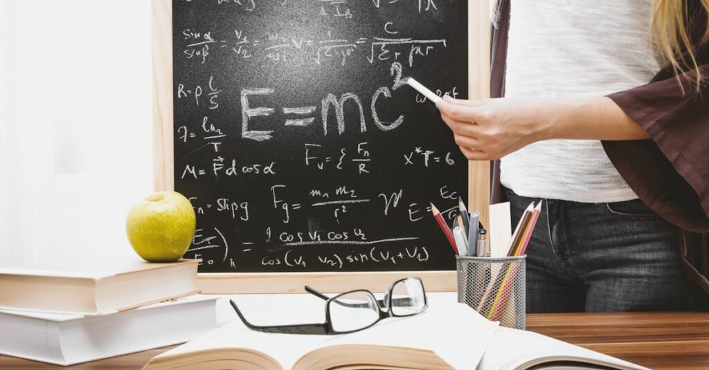 Woman writing physics equations on a blackboard with books and an apple on the desk.
