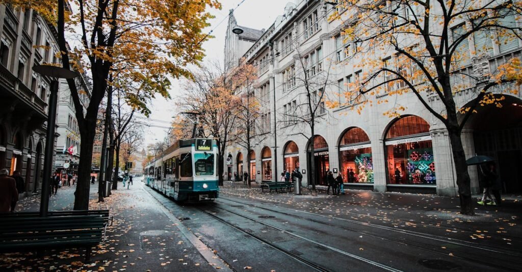 A tram travels down a leaf-strewn street in autumnal Zürich, Switzerland's urban landscape.