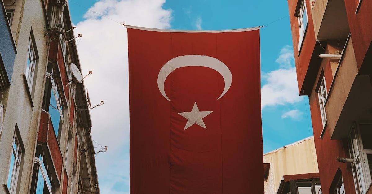 A Turkish flag hangs prominently between buildings under a bright blue sky in Sultangazi, Istanbul.
