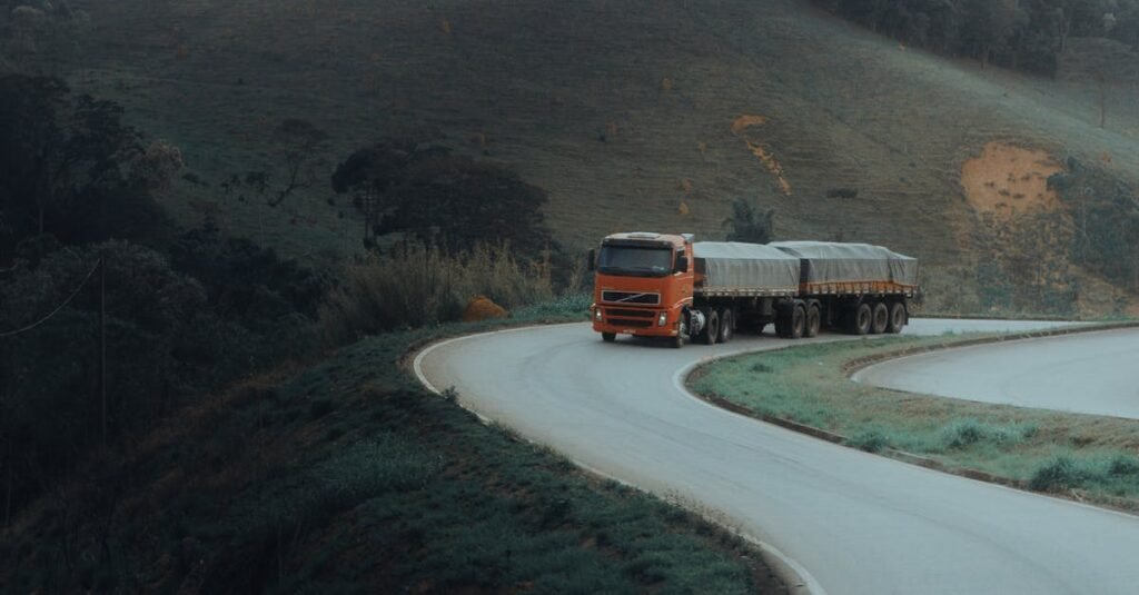 A red truck drives on a winding road in a mountainous landscape, showcasing scenic transportation.