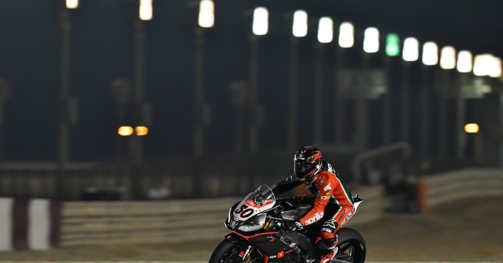 Motorcycle racer in action on the track at night, showcasing speed and skill under stadium lights.