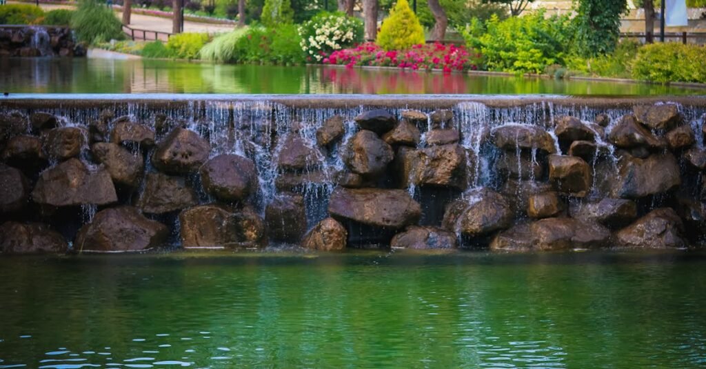 A serene waterfall over rocks in Şehitkamil Park, Gaziantep, surrounded by lush greenery and flowers.