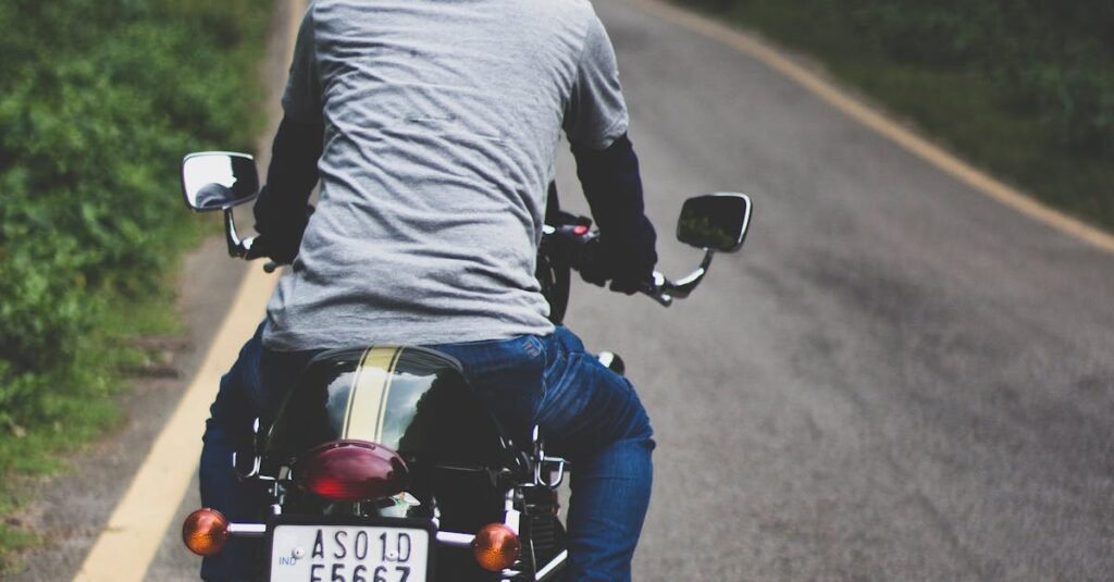 Man on motorcycle rides down a winding forest road on a clear day.