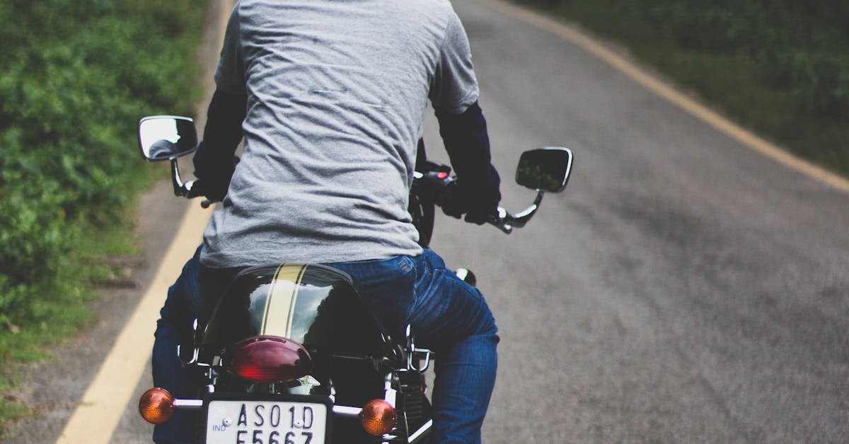 Man on motorcycle rides down a winding forest road on a clear day.