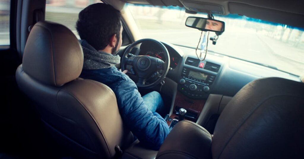 A man driving a car with focus on interior, dashboard, and steering wheel, captured from the backseat.