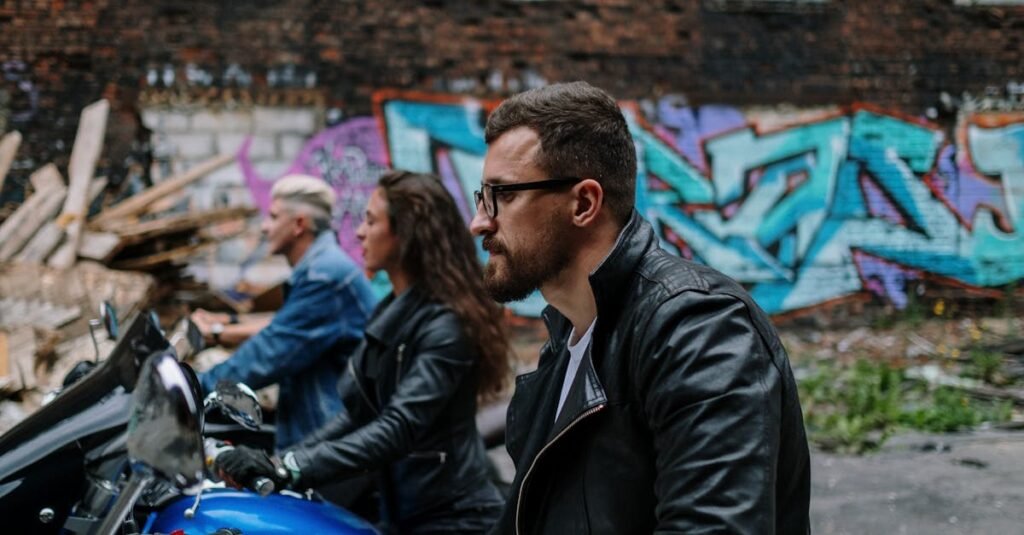A group of stylish bikers in leather jackets ride through a graffiti-covered urban setting.