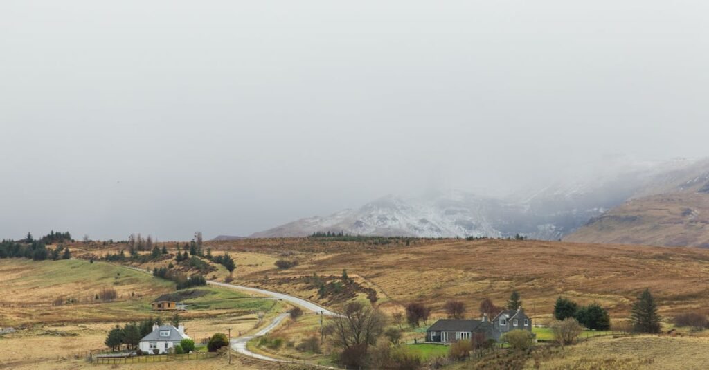 Foggy countryside in Scotland with houses and winding road amidst hills and mountains.