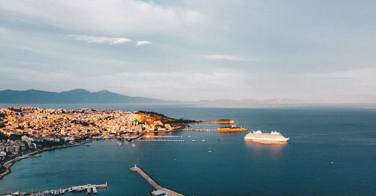 Aerial view of Kusadasi harbor with yachts and a cruise ship under a bright sky.