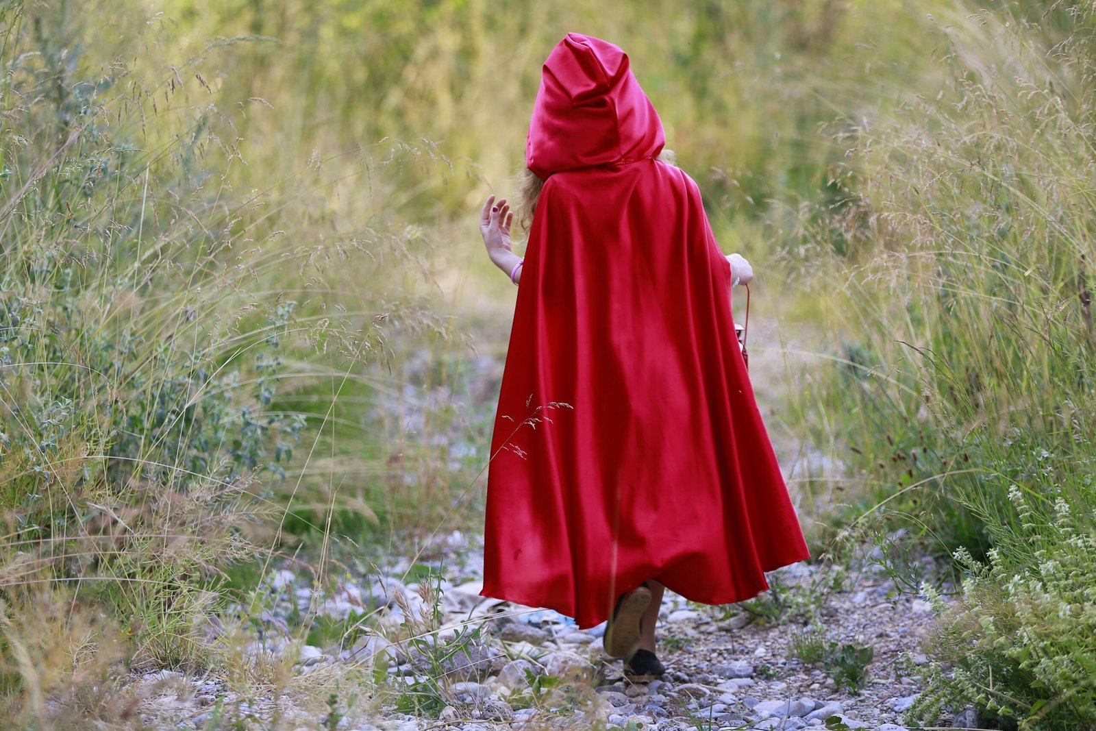 Person wearing a red cape walking in nature, evoking Little Red Riding Hood.
