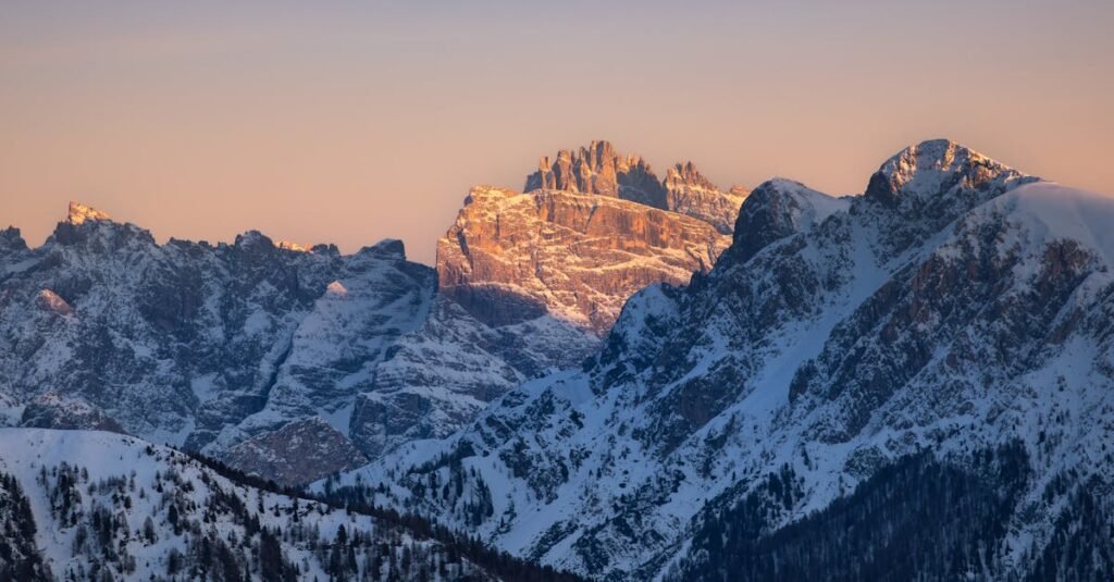 Snow-covered peaks of the Dolomites bathed in golden sunset light, showcasing winter's beauty in Italy.