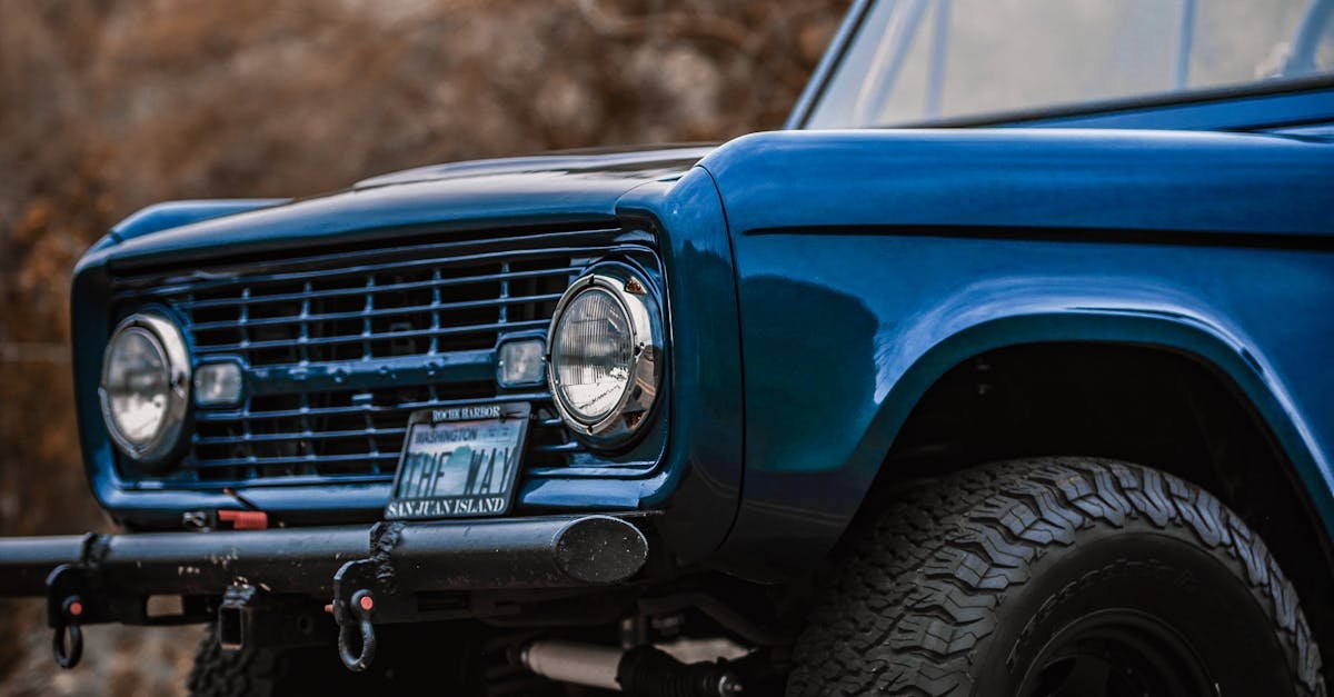 Vintage blue car captured on a scenic road with rugged terrain as the backdrop.