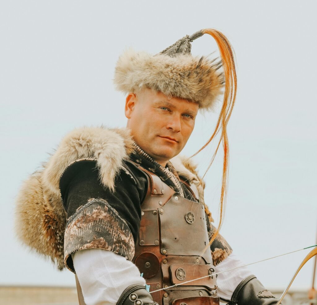 A man dressed in traditional Turkish warrior armor with fur details poses outdoors against a clear sky.