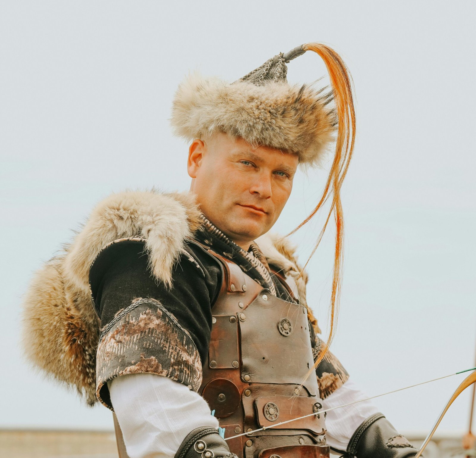 A man dressed in traditional Turkish warrior armor with fur details poses outdoors against a clear sky.