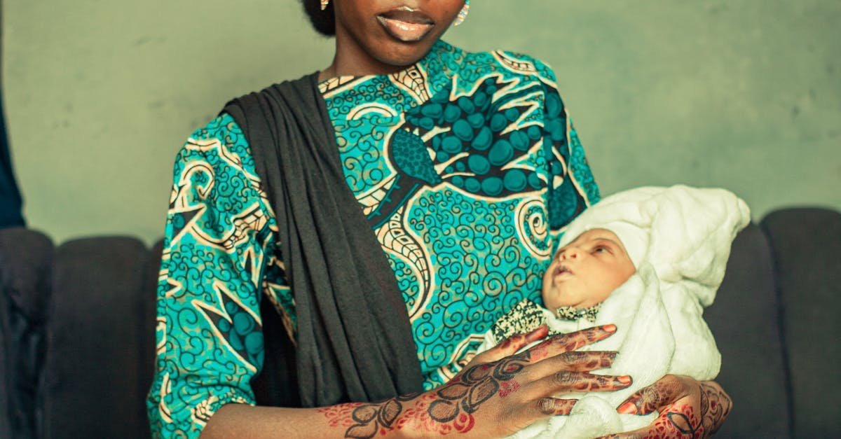 A mother holding her baby, both in traditional attire, sitting indoors.