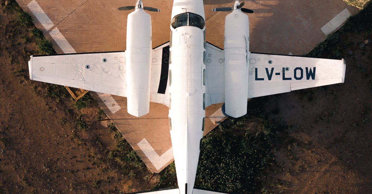Aerial top view of white airplane with propellers on edge of paved airfield in light