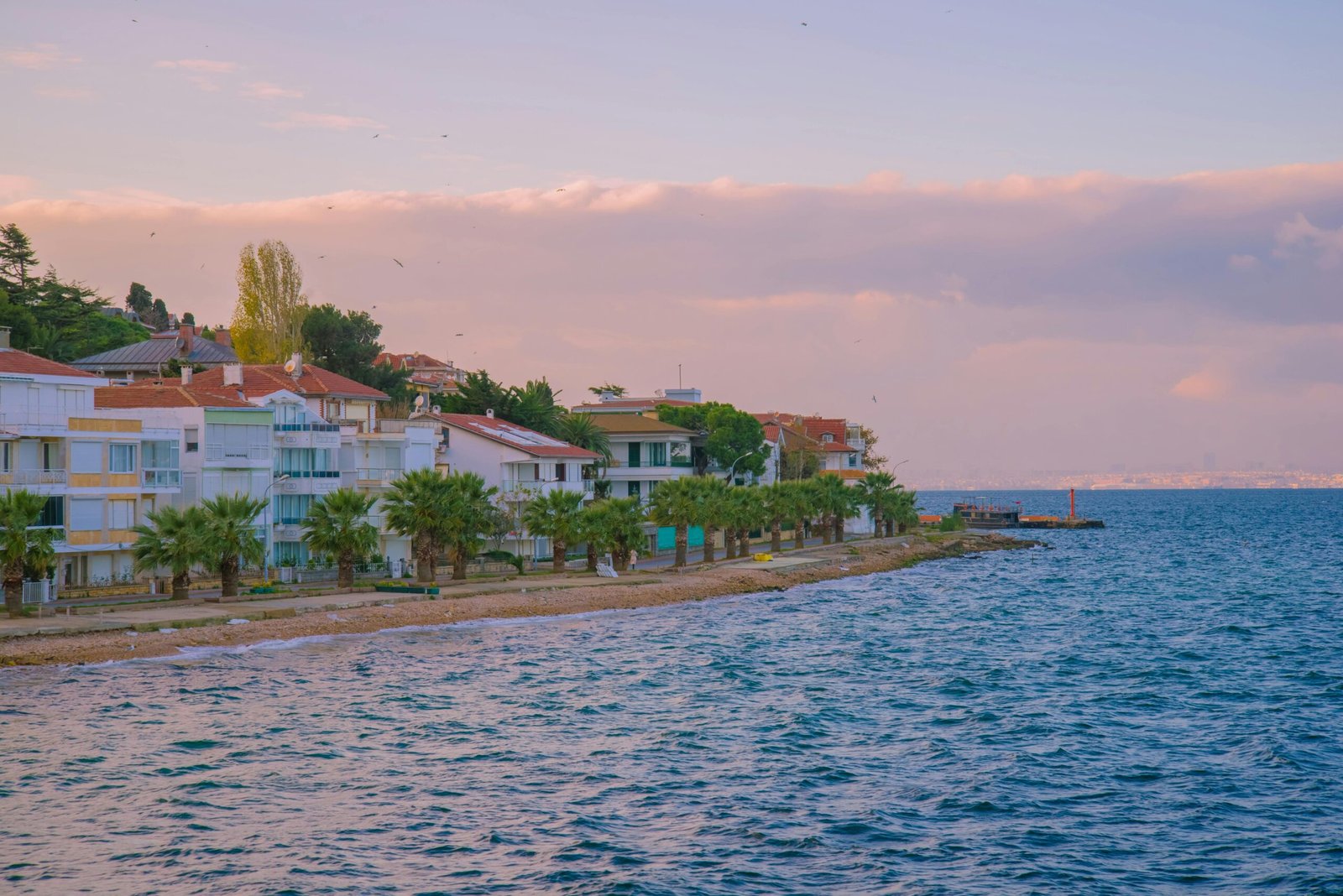 Beautiful view of a Turkish seaside town with palm trees and calm sea during sunset.