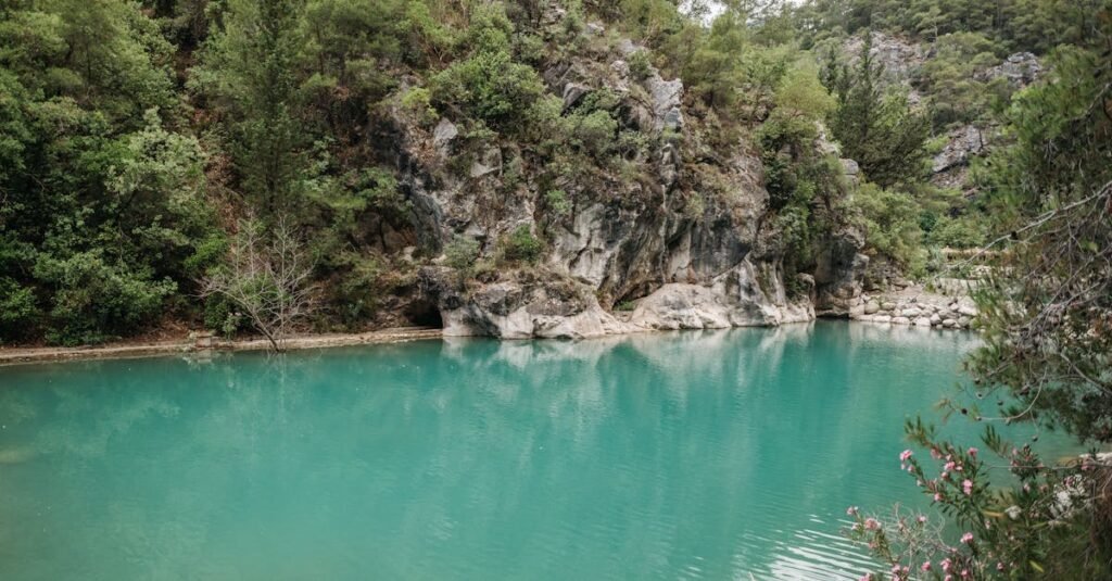 Tranquil turquoise lake surrounded by lush greenery and rocky cliffs in a serene natural setting.