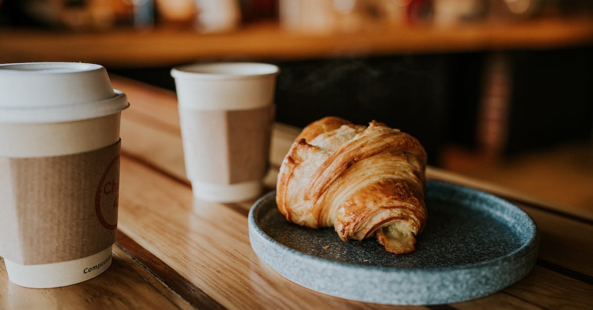 Cozy café setting with paper cup coffee and fresh croissant on a wooden table.