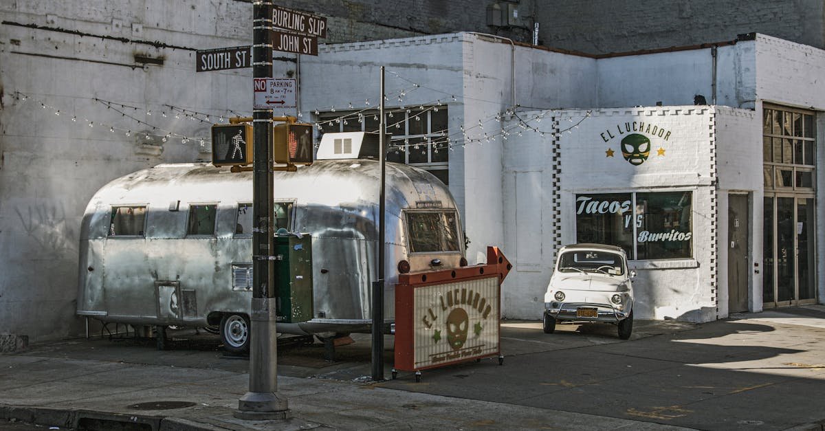 Rustic street scene in NYC with a vintage trailer, small car, and taco shop.