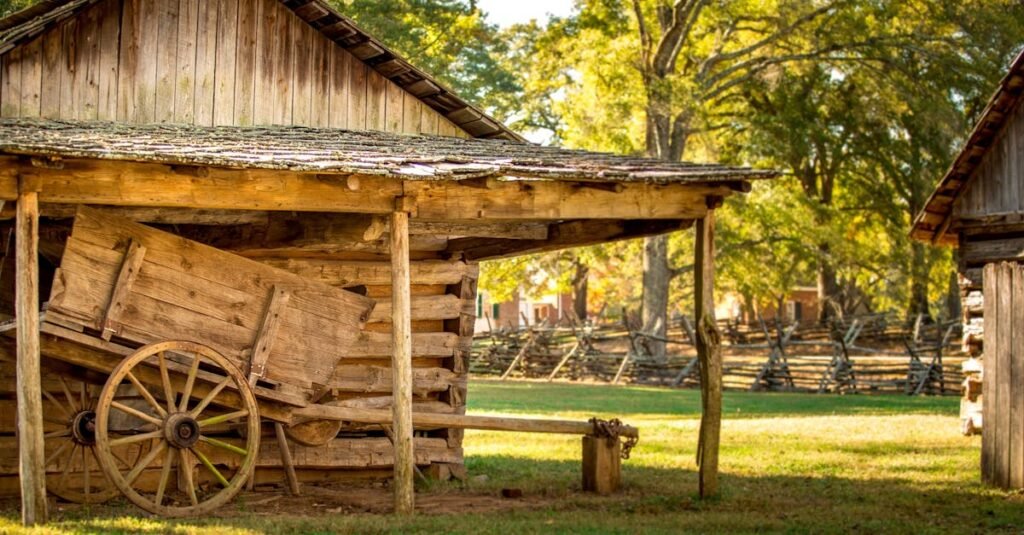 A rustic wooden barn with an old wooden wagon in a sunny outdoor farm setting.